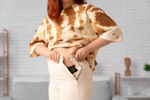 Image of woman trying to do her trousers up after pregnancy weight gain Stroud