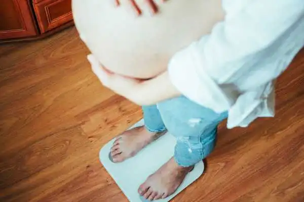 Image of woman weighing herself and experiencing weight gain through pregnancy Stroud